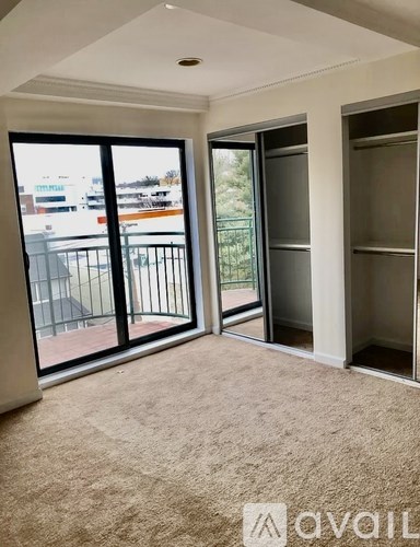 A room with a carpeted floor and a view of a parking lot through a glass door.