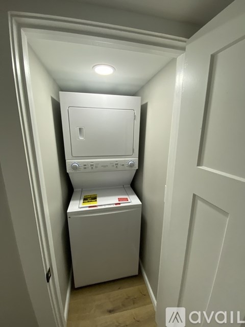 A small white washing machine sits in a narrow space between two walls.