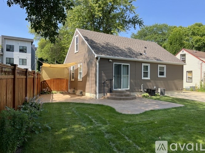 A house with a brown roof and a grey siding is surrounded by a green lawn.