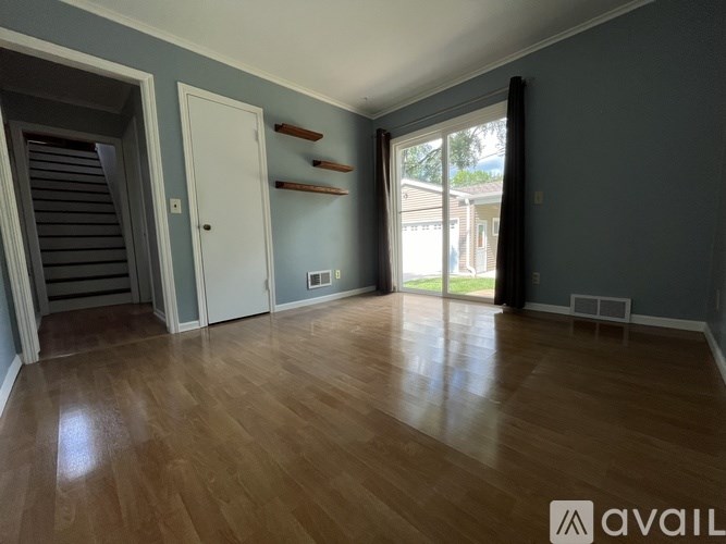 A room with wooden flooring and a sliding glass door leading to a balcony.
