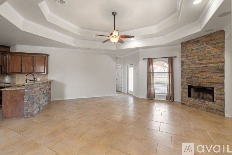 A spacious living room with a stone fireplace and a ceiling fan.