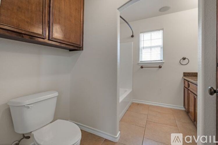 A bathroom with a toilet, a window, and wooden cabinets.
