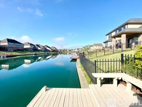 A wooden dock leads to a calm body of water with houses on the other side.