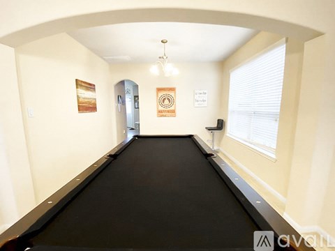 A room with a black pool table and a painting on the wall.