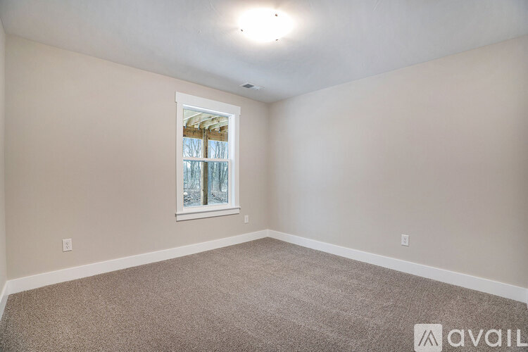 A room with a carpeted floor and a window with a view of trees outside.