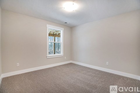 A room with a carpeted floor and a window with a view of trees outside.