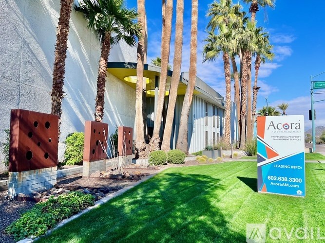 A sign for Acora Apartments is in front of a building with palm trees.