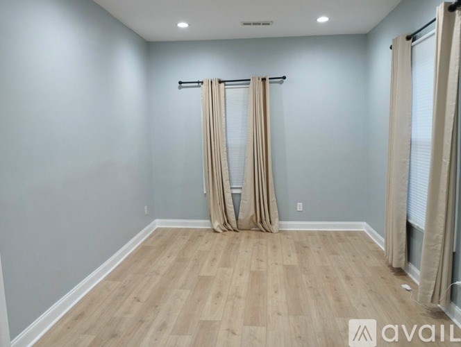 A room with light grey walls and wooden flooring, with a pair of beige curtains hanging on a rod.