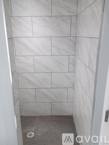 A white tiled shower with a drain in the middle.