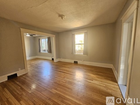 A room with wooden flooring and two windows.