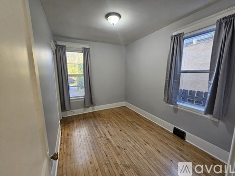 A room with wooden flooring and a window with grey curtains.