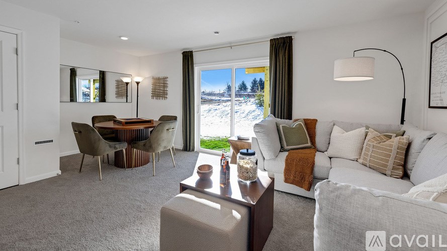 A living room with a grey carpet and a large window with a view of the snowy outdoors.