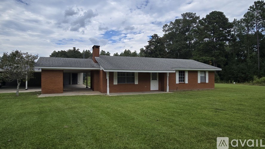 A house with a red brick exterior and a grey roof is surrounded by a grassy lawn.