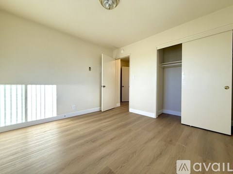A spacious room with wooden floors and white walls, with a door on the right and a window on the left.
