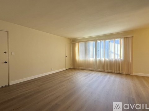 A spacious room with wooden flooring and a window with blinds.