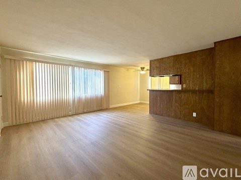 A spacious room with wooden flooring and a large window with blinds.
