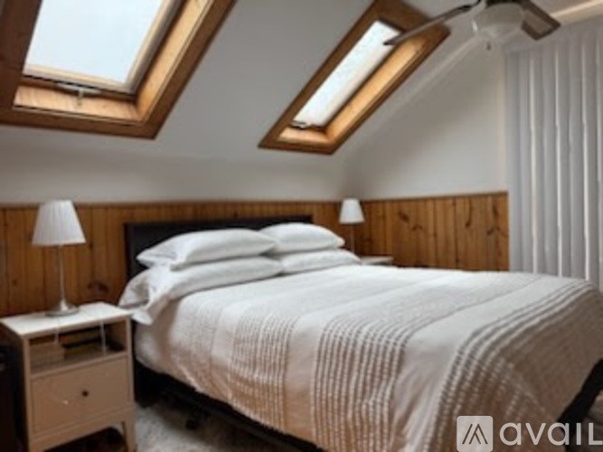 A bedroom with a bed, nightstand, and skylight.