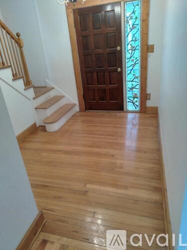 A wooden door with a glass panel is at the end of a hallway with wooden flooring and stairs.