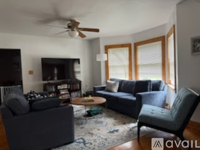 A living room with a grey couch, a blue armchair, a coffee table, and a ceiling fan.