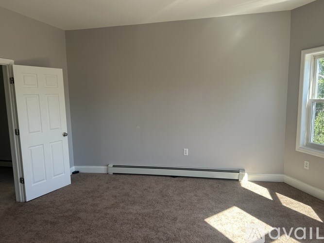 A room with a carpet floor, a door, and a window with sunlight coming through.
