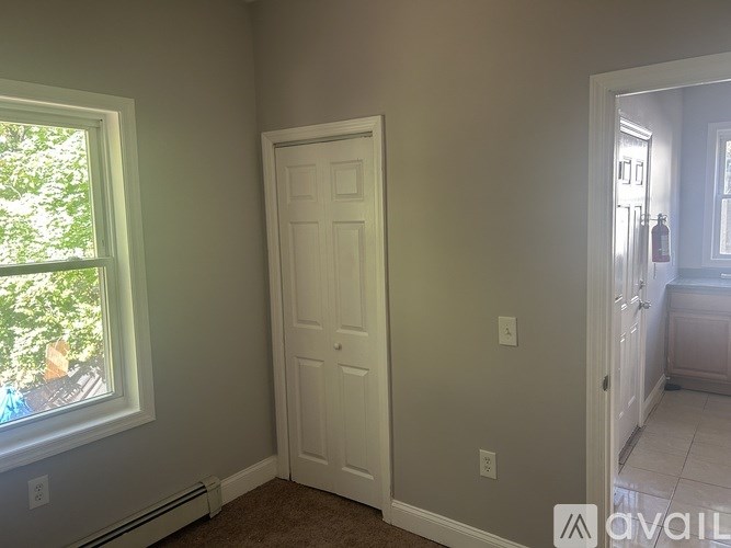 A room with a white door and a window with a view of trees and a house.
