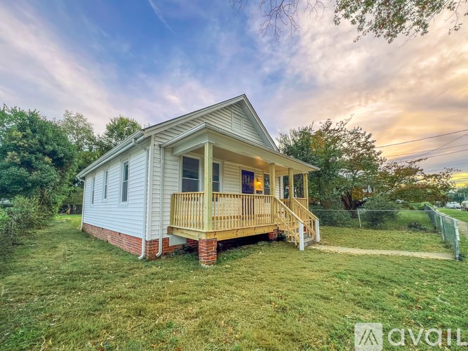 A small house with a porch is surrounded by greenery.