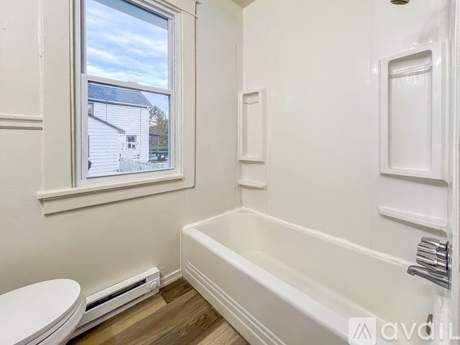 A white bathroom with a toilet, window, and bathtub.
