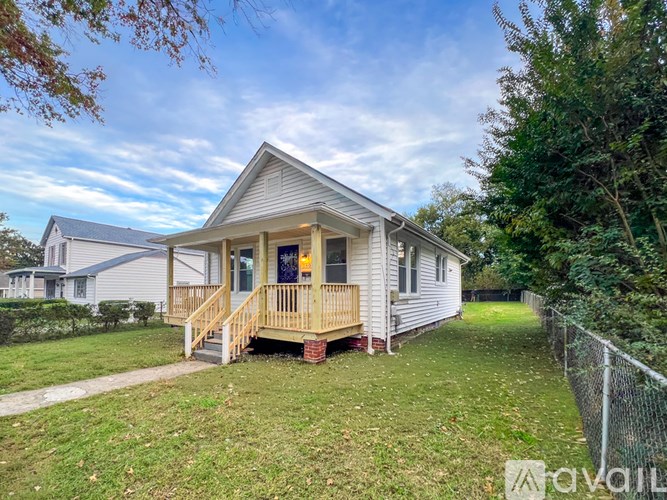 A small house with a porch is surrounded by a fence and trees.