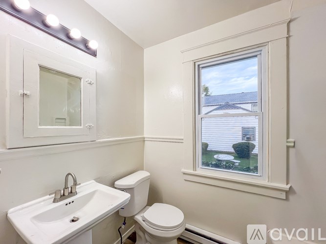 A bathroom with a white sink, toilet, and a window showing a view of a house.