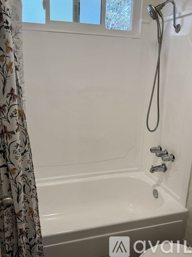 A white bathtub with a shower head and a curtain with a floral pattern.