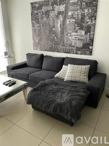 A black couch with a grey furry throw on it.