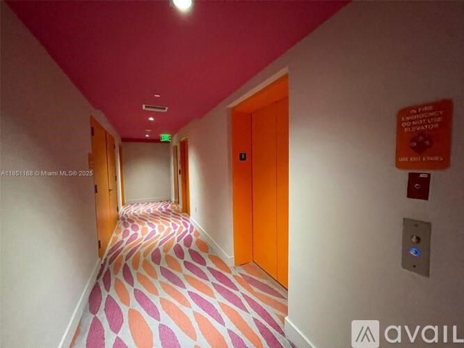 A hallway with a pink and orange carpet and a red sign on the wall.