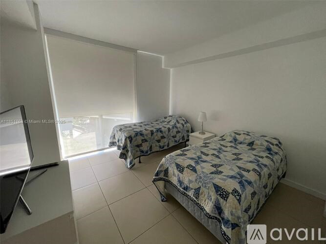 Two twin beds with blue and white bedspreads in a room with white walls and tiled floor.