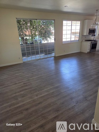 A room with wooden flooring and a kitchen area in the background.