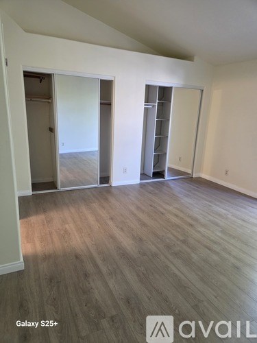 A room with wood flooring and white walls, with a door and a shelving unit visible.
