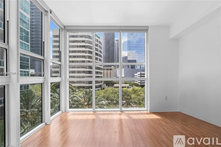 A spacious room with wooden floors and large windows overlooking a cityscape.