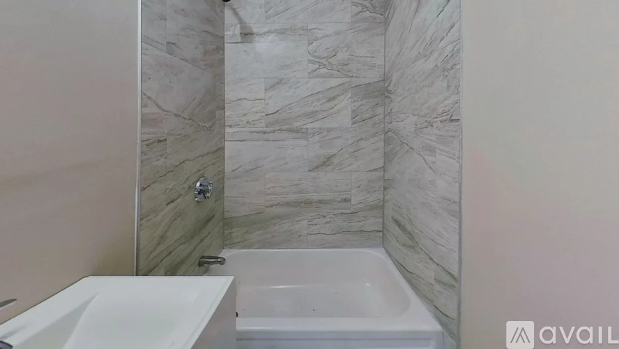 A bathroom with a marble tile wall and a white bathtub.
