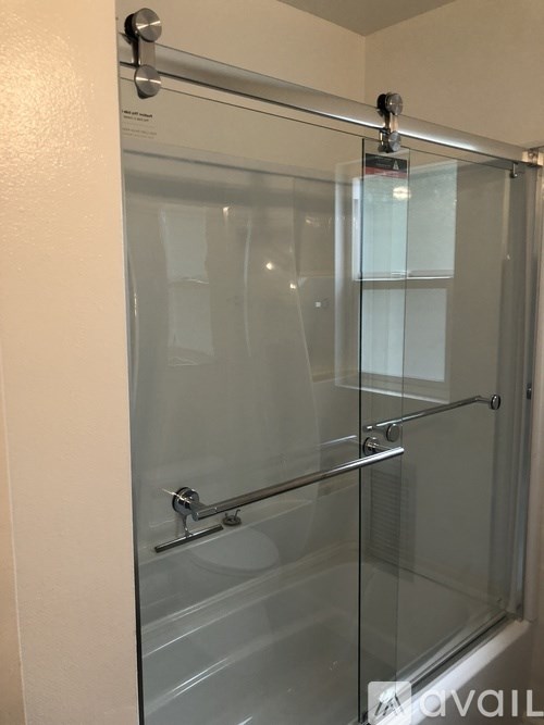 A glass shower door with a handle and a hinge.