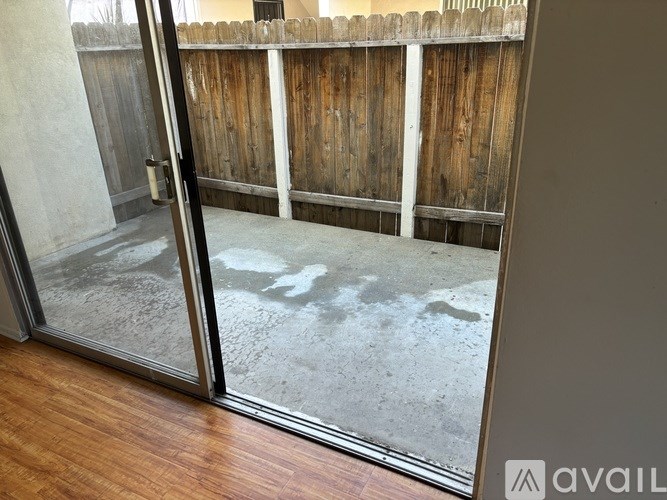 A glass door with a handle is open to a backyard with a wooden fence.
