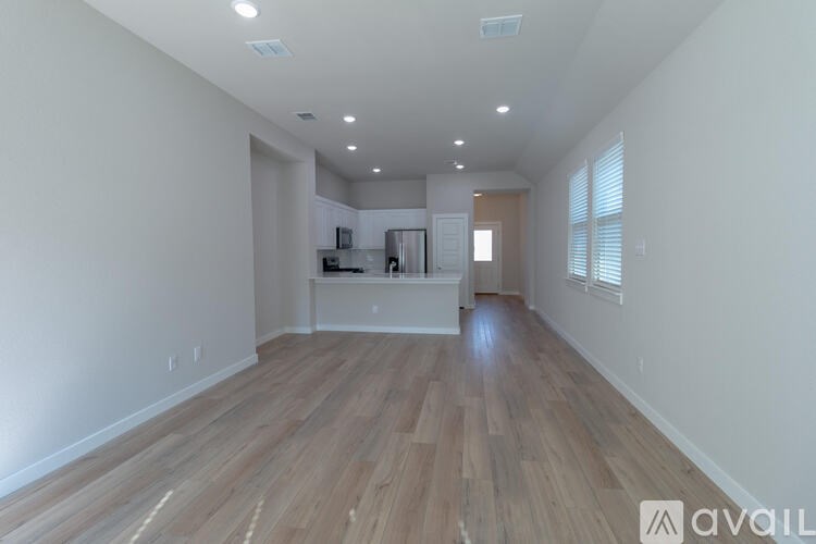 A spacious room with wooden flooring and a kitchen area in the background.