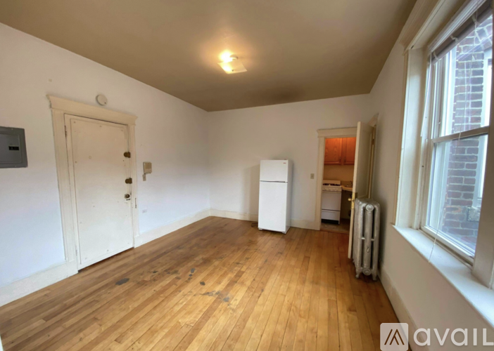 A room with wooden floors and white walls, with a door, a window, and a radiator.