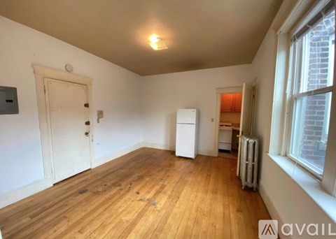 A room with wooden floors and white walls, with a door, a window, and a radiator.