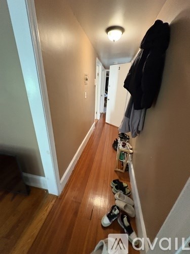 A hallway with shoes lined up on the floor and coats hanging on the wall.