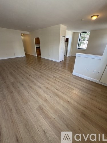 A room with wooden flooring and white walls, with a window on the right wall.