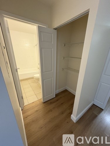 A white closet with shelves and a door open to a bathroom.