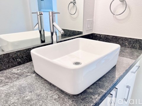 A white square sink with a drain in the middle is on a granite countertop.