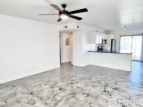 A spacious room with a ceiling fan and a kitchen area in the background.