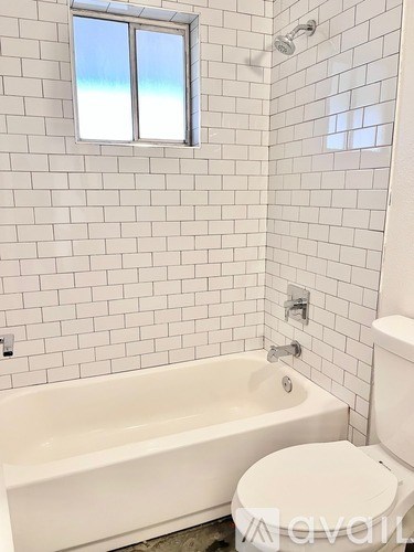 A white bathroom with a tub, toilet and window.