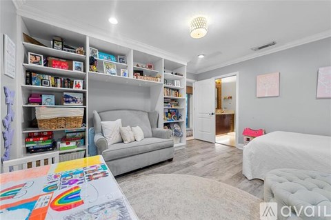 A living room with a grey couch, a white bed, and a bookshelf filled with books and toys.