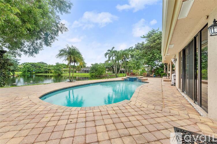 A swimming pool surrounded by a brick patio and a lush green landscape.